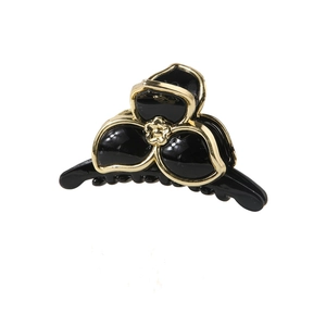 Détail d'une pince à cheveux en résine noire avec bords dorés et motif fleur centrale