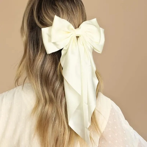 Macro detail of oversized creamy satin bow hair clip with elegant long ribbons on model