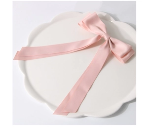 Barrette nœud en satin rose avec longs rubans sur une assiette en céramique blanche