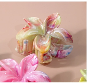 Vue détaillée de la pince à cheveux fleur en acétate avec texture marbrée sur fond rose