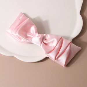 Fermaglio per capelli con fiocco in raso rosa e consistenza setosa su piatto bianco