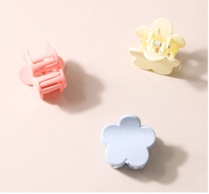 Three-piece set of matte flower hair clips in pink yellow and blue on a soft pink surface