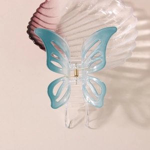 Pince à cheveux papillon bleue évidée avec ressort doré sur un plateau de coquillage