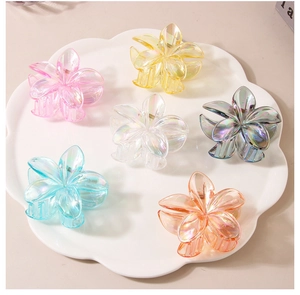 Vue à plat de six pinces à cheveux en forme de fleur de frangipanier irisée sur plat blanc
