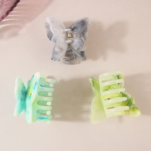 Three butterfly hair claws in marble acetate finish with spring mechanism on pink surface
