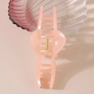 Close-up of pink translucent wavy hair claw clip with golden metal spring on shell tray