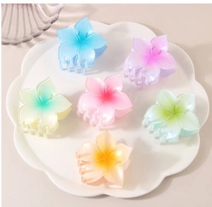 Detail view of 6 colorful gradient plumeria hair claws arranged in a white ceramic plate