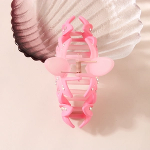 Pink matte hair claw clip with rhinestones and flower design on a seashell tray