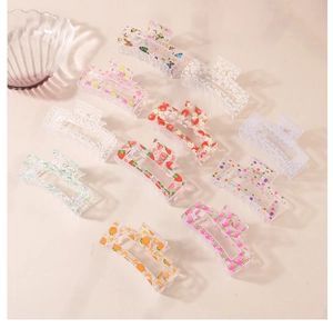Flat lay of large acrylic hair claws with floral and fruit patterns on beige background