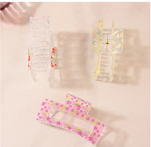 Three acrylic hair claws featuring cherry, lemon, and floral prints on a beige surface