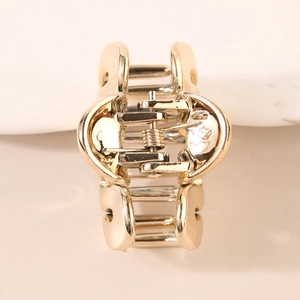 Minimalist golden metal hair claw clip with a polished mirror finish on a plain background