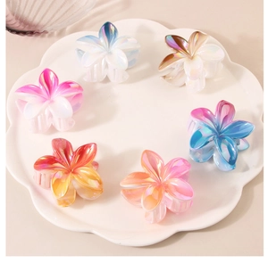 Detailed macro view of six pearlescent plumeria flower hair claws in a decorative white tray