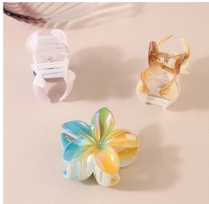 Detailed macro view of three iridescent plumeria and geometric resin hair claw clips
