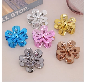 Close-up of set of six metallic floral claw clips in assorted colors on pink surface
