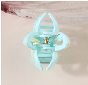 Detail view of a matte cyan hair claw clip featuring golden springs and petal design