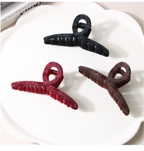 Three large flocked hair claws in black, burgundy, and dark brown on a ceramic tray