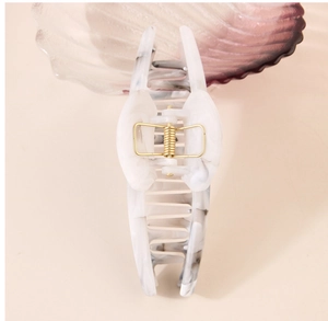 Detail view of large marble acrylic hair claw clip with golden metal spring mechanism