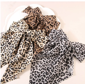 Three large leopard print bow hair clips with long ribbons on a white ceramic plate