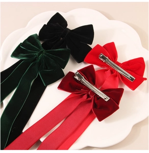 Detail view of velvet bow hair clips in green, black, and red with long streamers