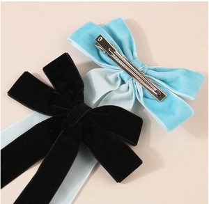 Detail of velvet ribbon bows in black and blue with metal duckbill clips on beige surface