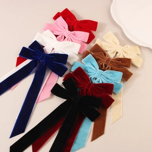 Elegant multi-color velvet bow hair clips with long ribbons arranged on a beige surface