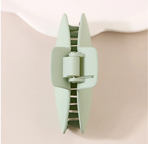 Close-up of matte light green plastic hair claw clip with metal spring on beige surface