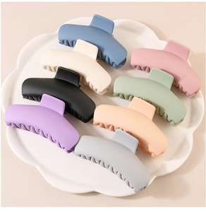 Macro detail of eight matte macaron-colored plastic hair claws arranged in a white tray