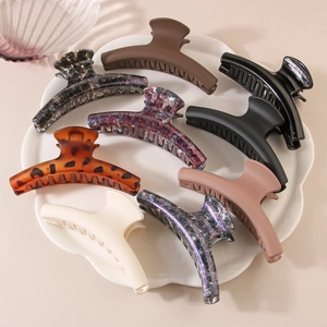Various stylish hair claws in matte and marble finishes displayed on a white ceramic tray