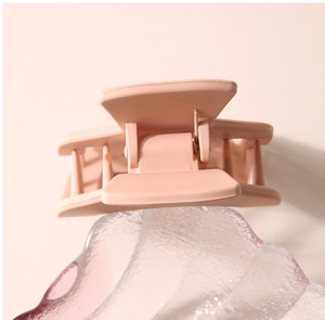 Gros plan détaillé d'une pince à cheveux carrée mate beige sur une surface en verre dépoli