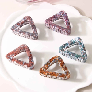 Five geometric triangle hair claw clips in marbled acetate textures on a white ceramic plate