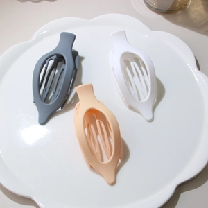 Close-up of matte resin hair claws in grey, beige, and peach pink on a ceramic tray