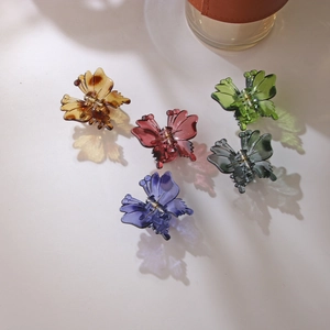 Group of colorful translucent butterfly hair claws with shadows on a beige surface