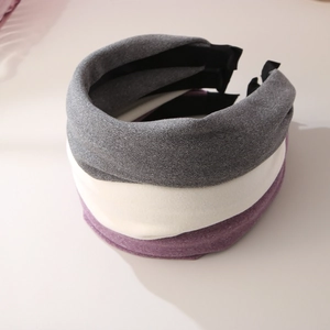 Close-up of three wide knitted headbands in grey, beige and purple with crossed texture