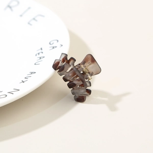 Detail of small tortoiseshell hair claw clip with metal spring on white porcelain plate