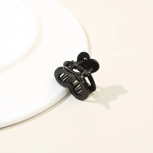 Detail shot of the glossy black heart-shaped mini hair claw clip on a white plate