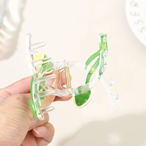Handheld view of a transparent avocado hair claw clip with green and yellow accents