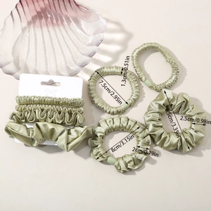 Detailed view of six green satin scrunchies in various sizes with silk-like sheen texture