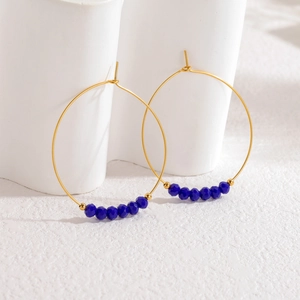 Orecchini a cerchio geometrici dorati con perline sfaccettate blu su fondo bianco