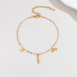 Bracelet minimaliste en acier doré avec breloques cœur os et plume sur fond blanc pur