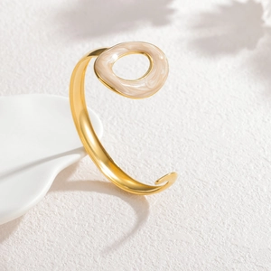 Detail shot of a minimalist gold open bangle with a white marble texture enamel oval charm