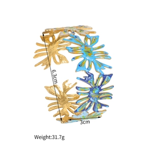 Vue détaillée d'un bracelet large en acier doré avec motifs de fleurs en émail bleu