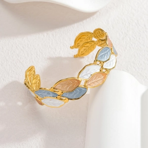 Elegant adjustable gold cuff bracelet with colorful enamel leaves on a white stand