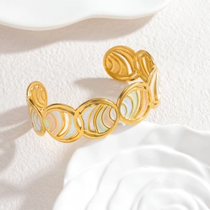 Detailed close-up of gold hollow bangle featuring colorful enamel circles on white tray