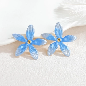 Détails macro de boucles d'oreilles fleurs bleu clair à cinq pétales et centre doré