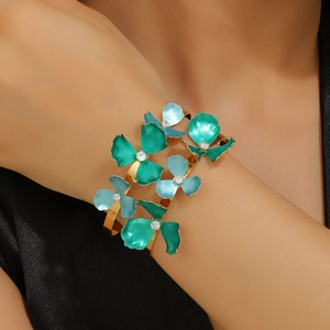 Golden open bangle with blue enamel flowers and sparkling crystals on model's wrist