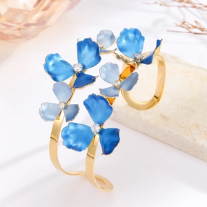 Detailed close-up of golden open cuff bracelet with blue enamel flowers and diamonds