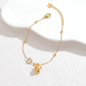 Detalle de pulsera de acero dorado con dije de hongo y circonita en forma de corazón