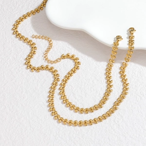 Golden wheat-ear style stainless steel necklace with leaf-shaped links on white textured surface