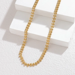 Detailed close-up of golden wheat-link stainless steel necklace on white stone blocks