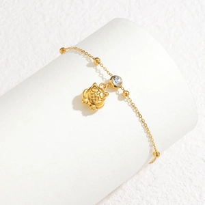 Detalle de pulsera de cadena dorada con circonita y dije de gato en soporte blanco